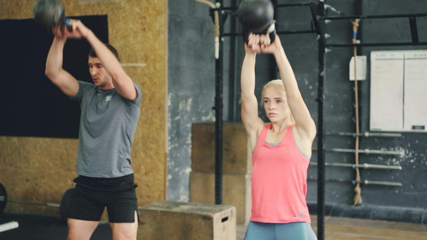 Mann og kvinne svinger kettlebells i en treningssal