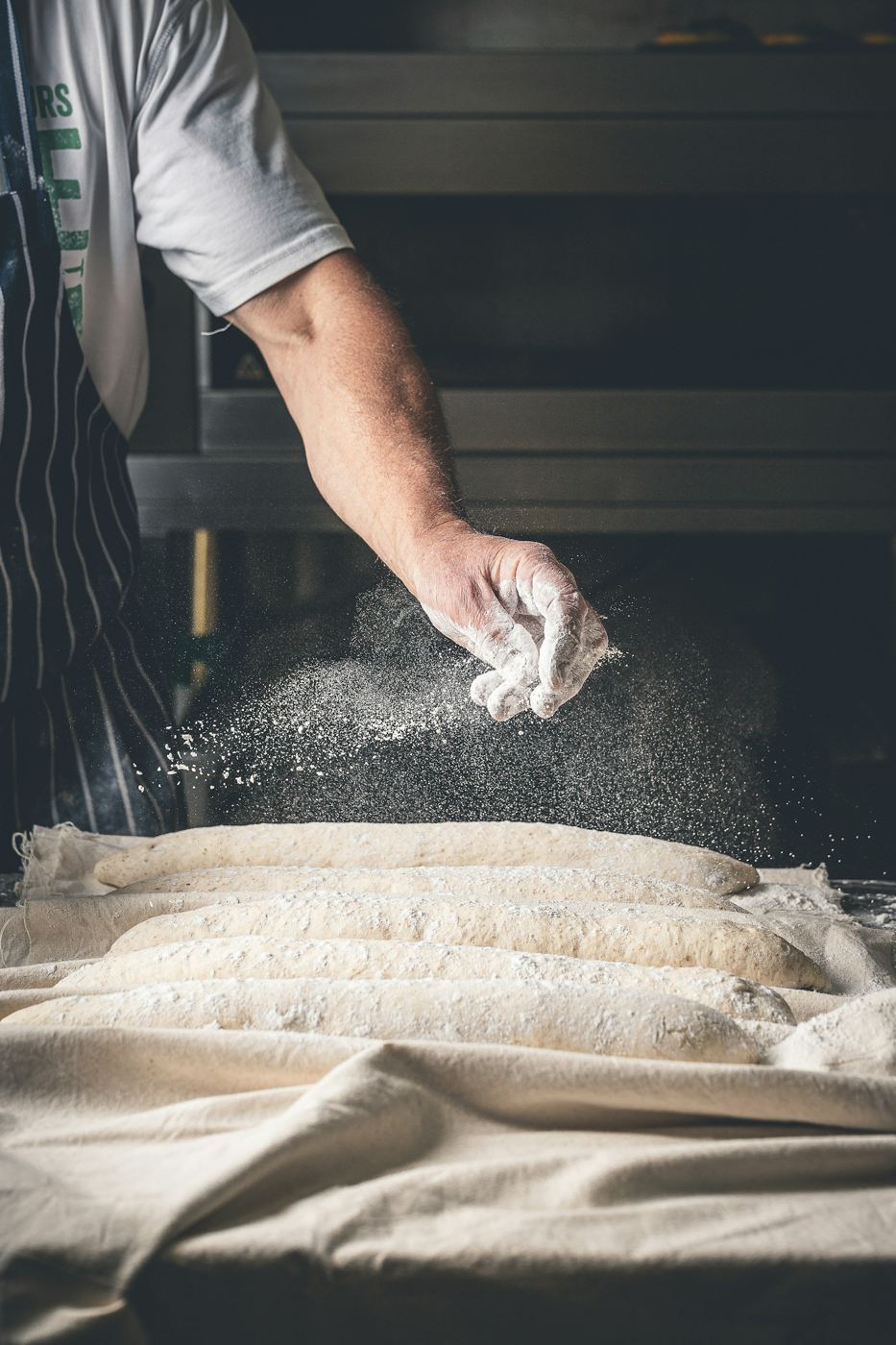 Baker drysser mel over baguetter som hever